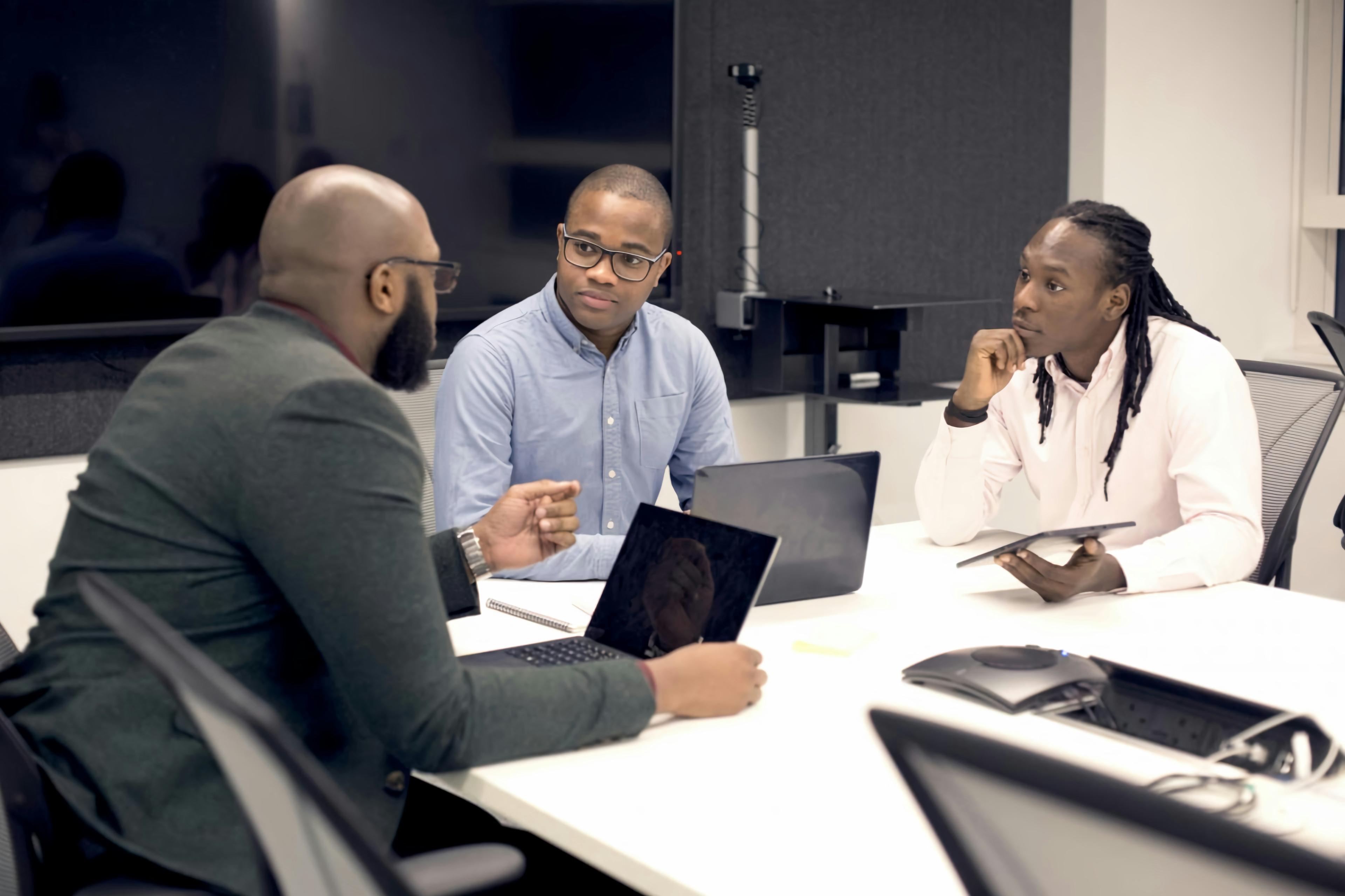 Three colleagues in a working session around a table with laptops